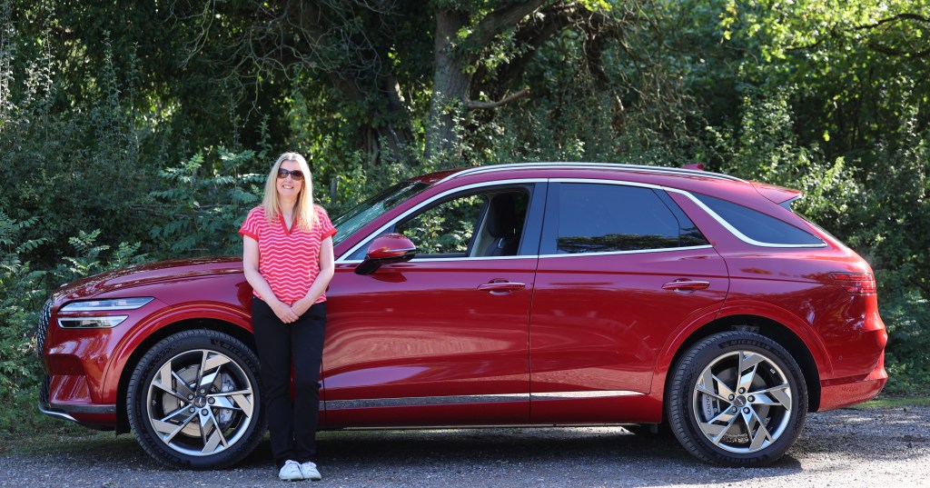 Tina Milton stands by a red Genesis Electrified GV70 for her long term review - side view of the car