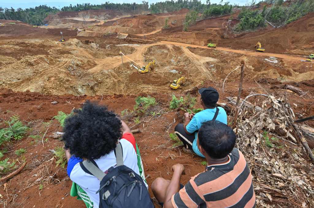 This picture taken on February 8, 2023 shows coconut farmer Hastoma (front R) and other farmers, whose lands were illegally taken by Gema Kreasi Perdana (GKP), looking at a nickel mining site operated by the company on Wawonii island, southeast Sulawesi. - The dig site is part of a huge rush to Indonesia, the world's largest nickel producer, by domestic and foreign enterprises to mine the critical component used in electric vehicle batteries. (Photo by Adek BERRY / AFP) / TO GO WITH "Indonesia-rights-mining-environment-China", FOCUS by Marchio GORBIANO (Photo by ADEK BERRY/AFP via Getty Images)