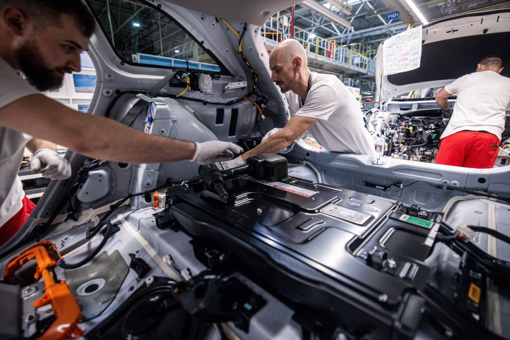 Workers install an electric battery inside a Kia Ceed Sportswagon plug-in hybrid electric vehicle (PHEV) on the assembly line at the Kia Slovakia sro plant in Zilina, Slovakia, on Friday, Oct. 27, 2023. European auto sales maintained double-digit growth in September despite higher interest rates raising the cost of acquiring a car. Photographer: Akos Stiller/Bloomberg via Getty Images