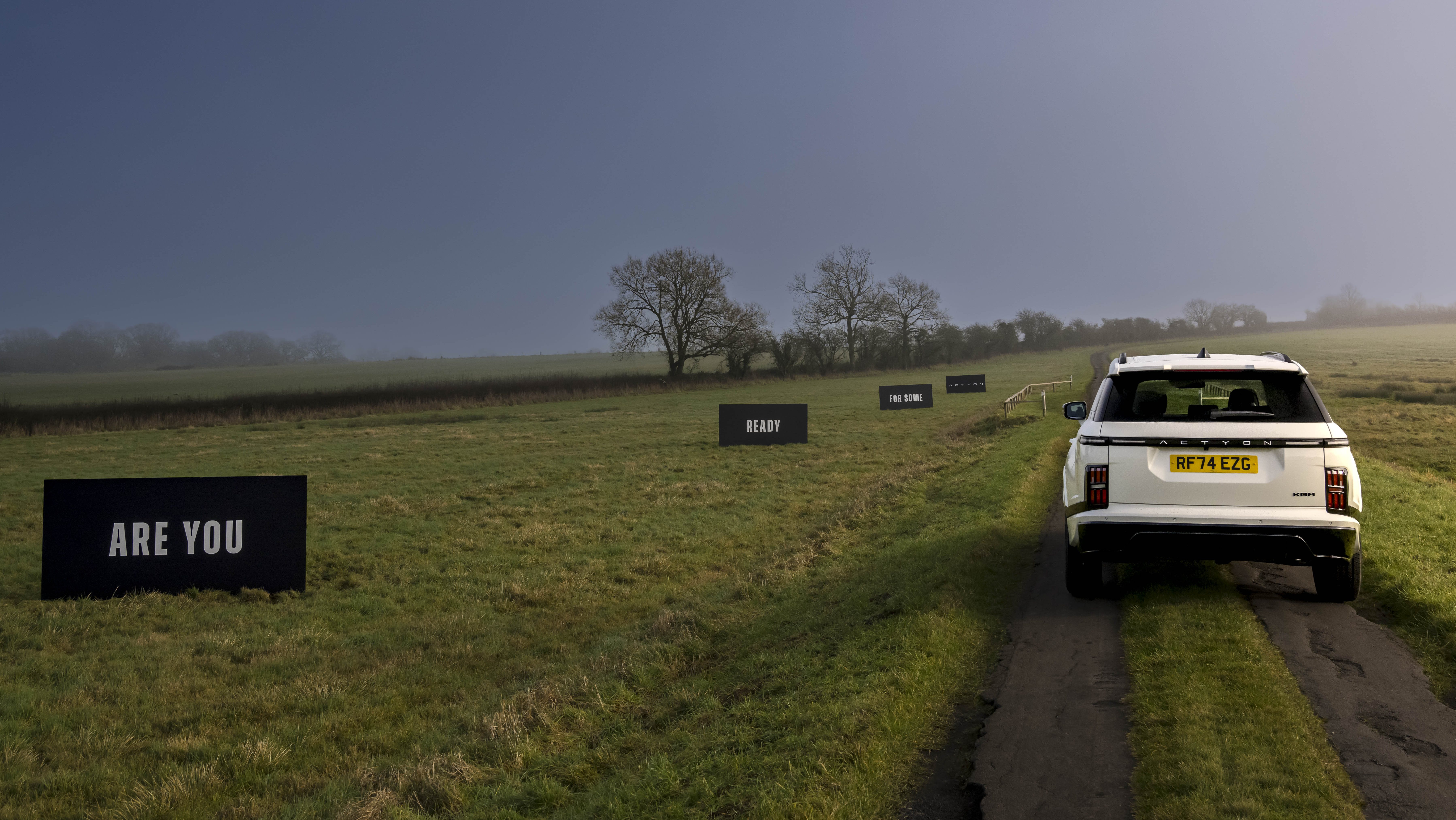 Rear view of KGM Actyon at UK launch, with roadside boards saying, “ARE YOU… READY… FOR SOME… ACTYON”